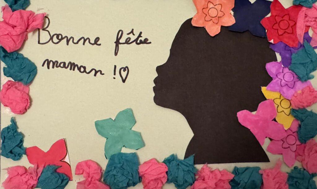 Collage de Fête des Mères réalisé par les enfants à la MAM Super Poppins de Blagnac. La carte montre une silhouette noire décorée de fleurs en papier multicolores et le message manuscrit "Bonne fête maman